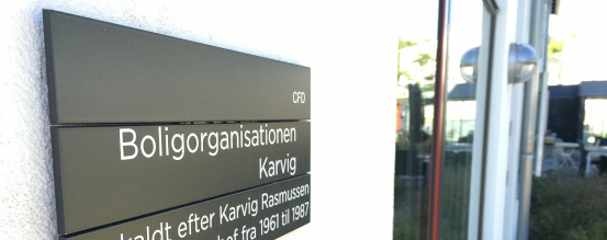 På billedet ses et skilt på en hvid mur. På skiltet står Boligselskabet Karvig.